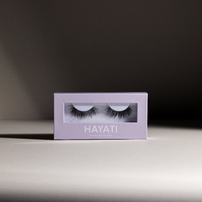 a product image with a contrasting background of cold gray and dark gray colors to make hayati lashes purple pacakging pop with the fluffy and lightweight cat eye lashes in the packaging 